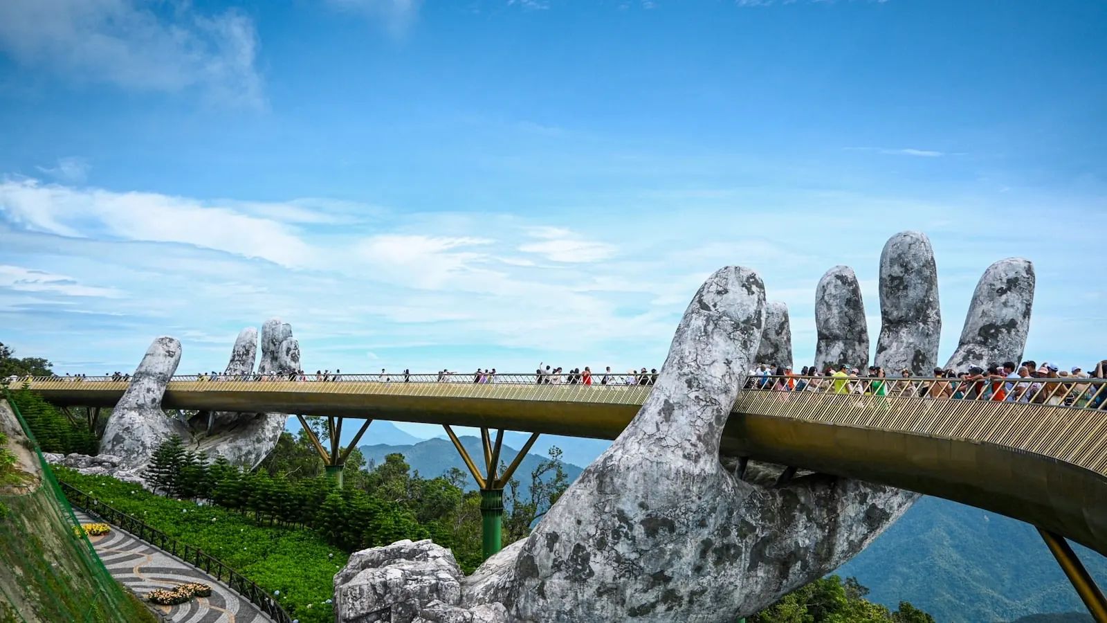 Cầu Vàng ở Bà Nà Hills uốn cong trên hai bàn tay đá khổng lồ, du khách đi bộ trên cầu giữa nền trời xanh