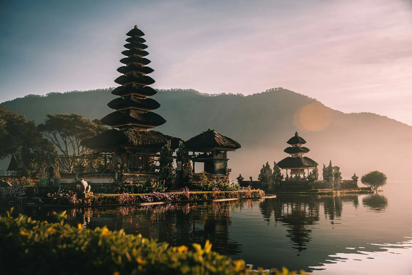 Đền Ulun Danu Beratan với các tháp mái tầng dựng bên mép hồ Bratan lúc sáng sớm, núi mờ phía sau