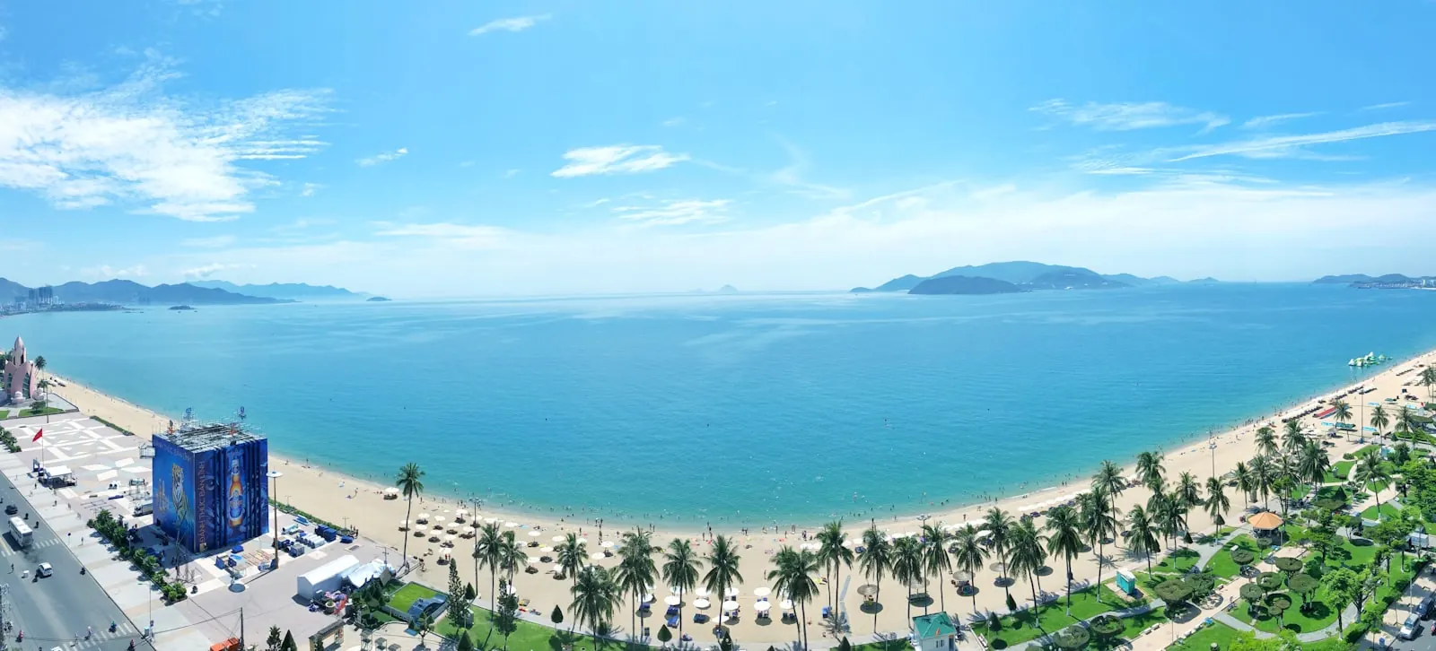 Bờ biển Nha Trang nhìn từ trên cao với hàng dừa dọc bãi cát, thành phố phía sau và các đảo nhỏ ngoài khơi