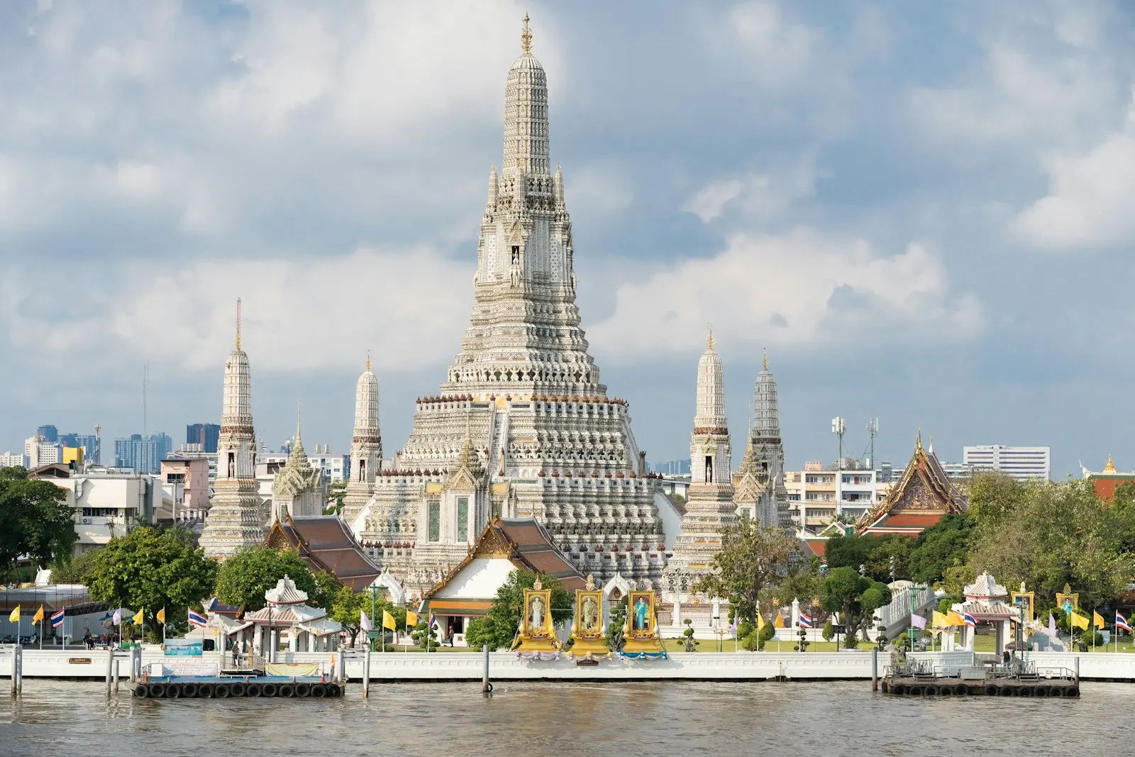 Chùa Wat Arun bên sông Chao Phraya ở Bangkok với tháp prang trung tâm nhọn và các tháp nhỏ vây quanh dưới nền trời nhiều mây